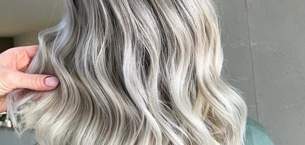 Hinterkopf einer Frau in grÃ¼nem Pullover mit blonden, gelockten Haaren die mit Balayagetechnik gefÃ¤rbt wurden